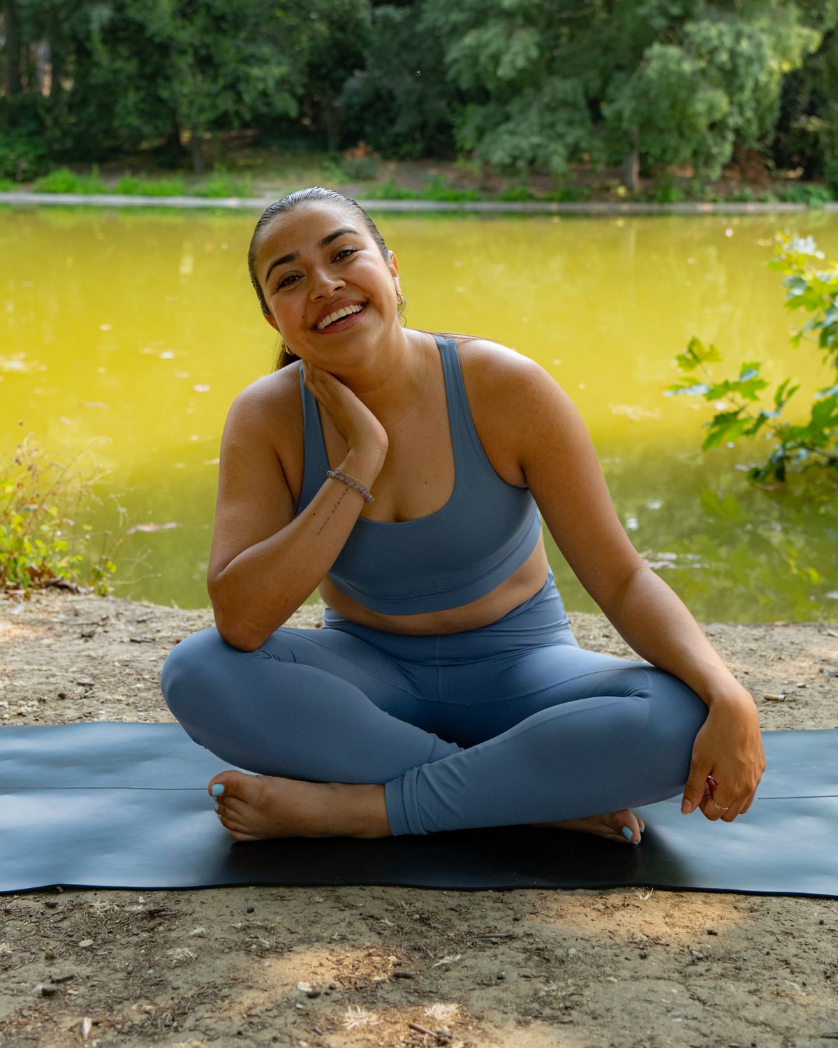 Hilary smiling on her yoga mat beside a lake in Paris